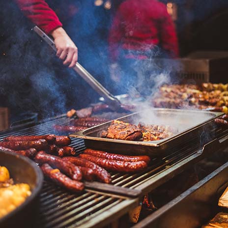 Outdoor street food festival. Chief cooking sausages, meat and potatoes cooking on an outdoor griddle